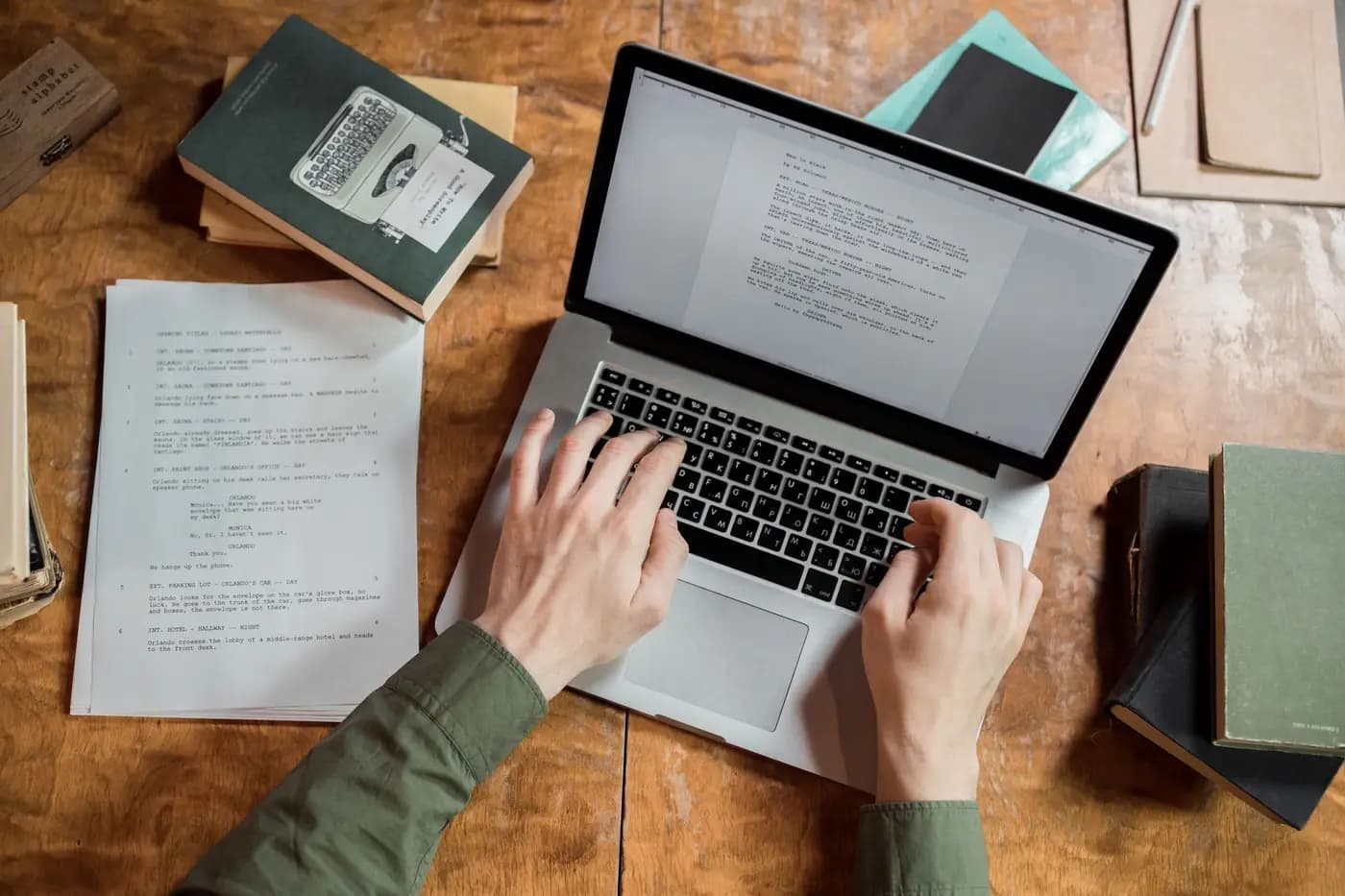 Writer working on a laptop, surrounded by books and manuscripts